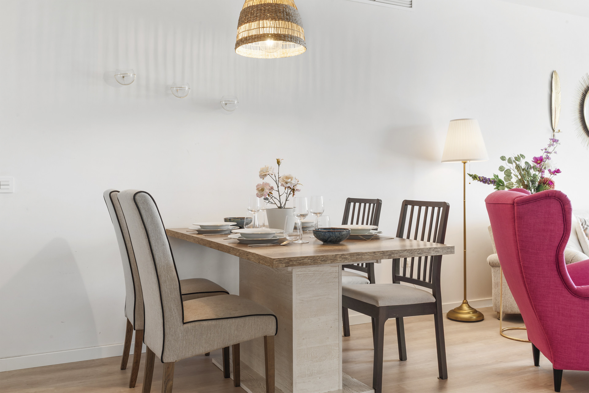 Dining area with a wooden table set for four, varied chairs, and a pink armchair in the background.