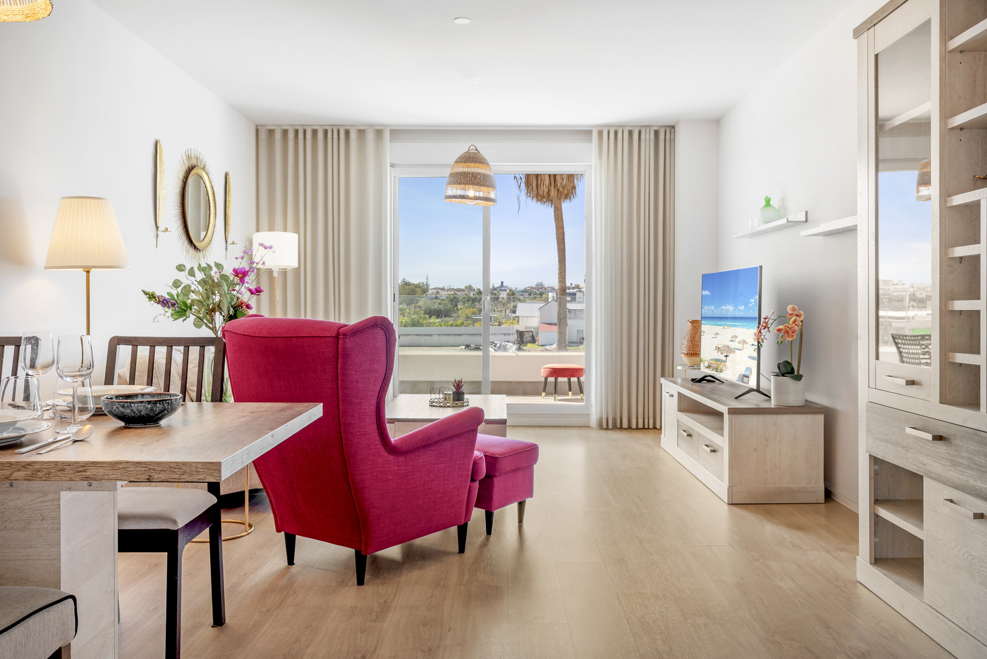 Combined living and dining room with a magenta armchair, TV, and balcony view of a town.