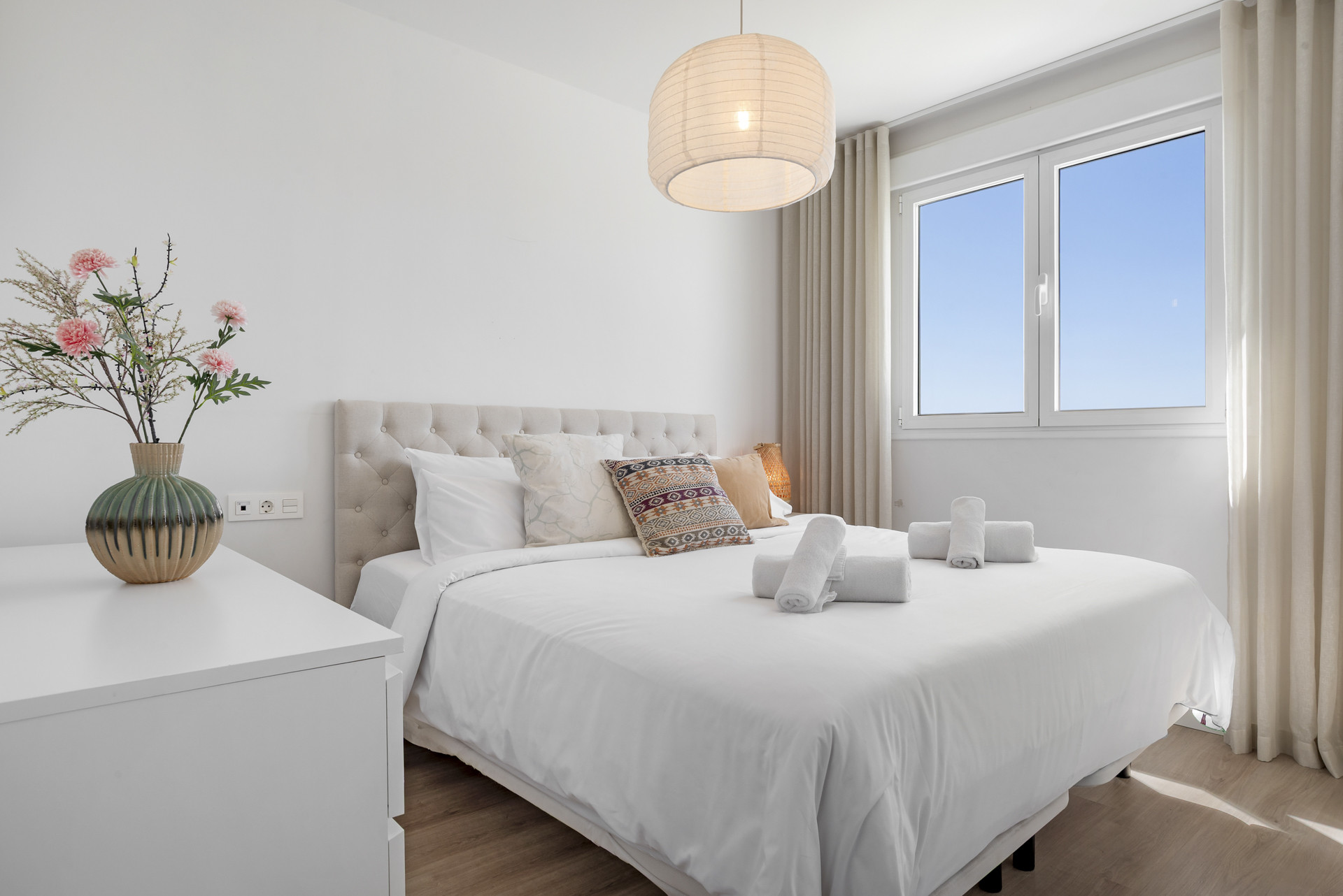 Bedroom with a large bed, white bedding, patterned pillows, a bedside table, and a window.