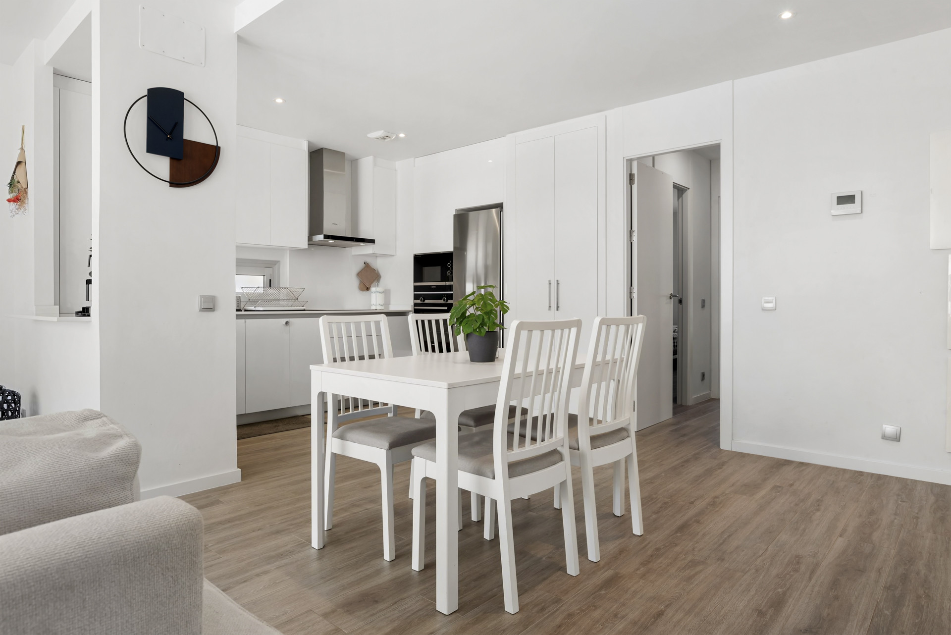 View of a modern white kitchen and dining area with a table, chairs, and a plant.