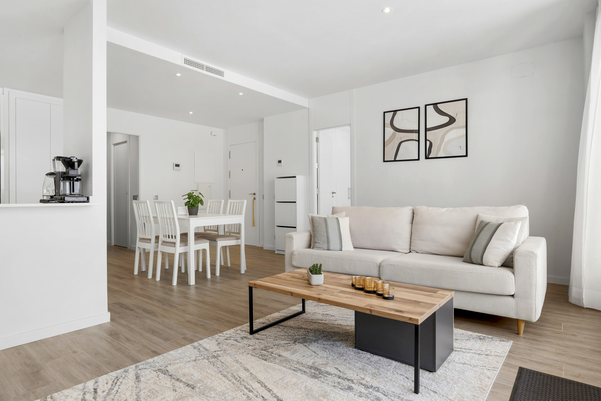 Open concept living and dining area with a light sofa, wooden coffee table, and white dining set.