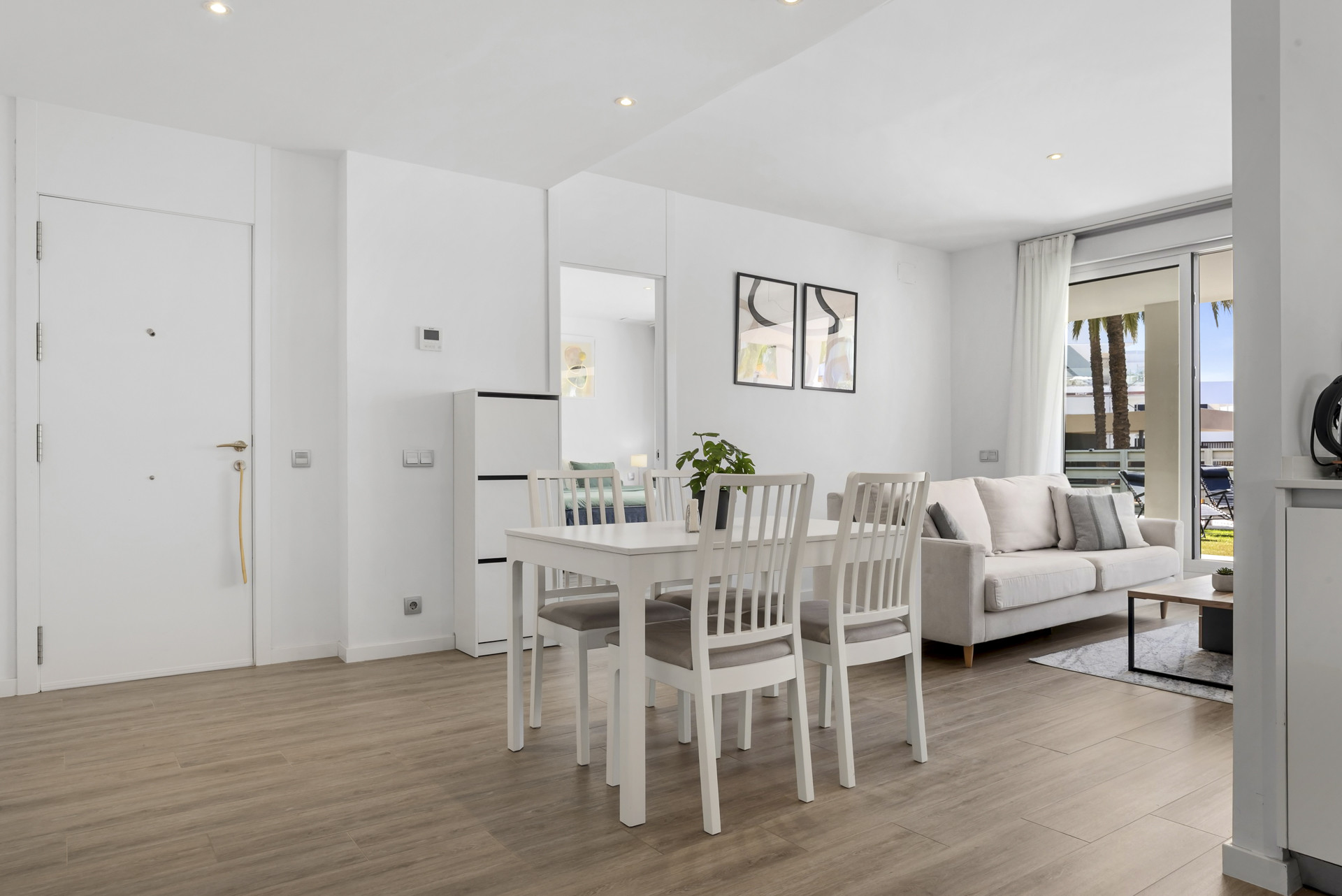 Dining area with a white table and chairs, visible door to a bedroom, and living area beyond.