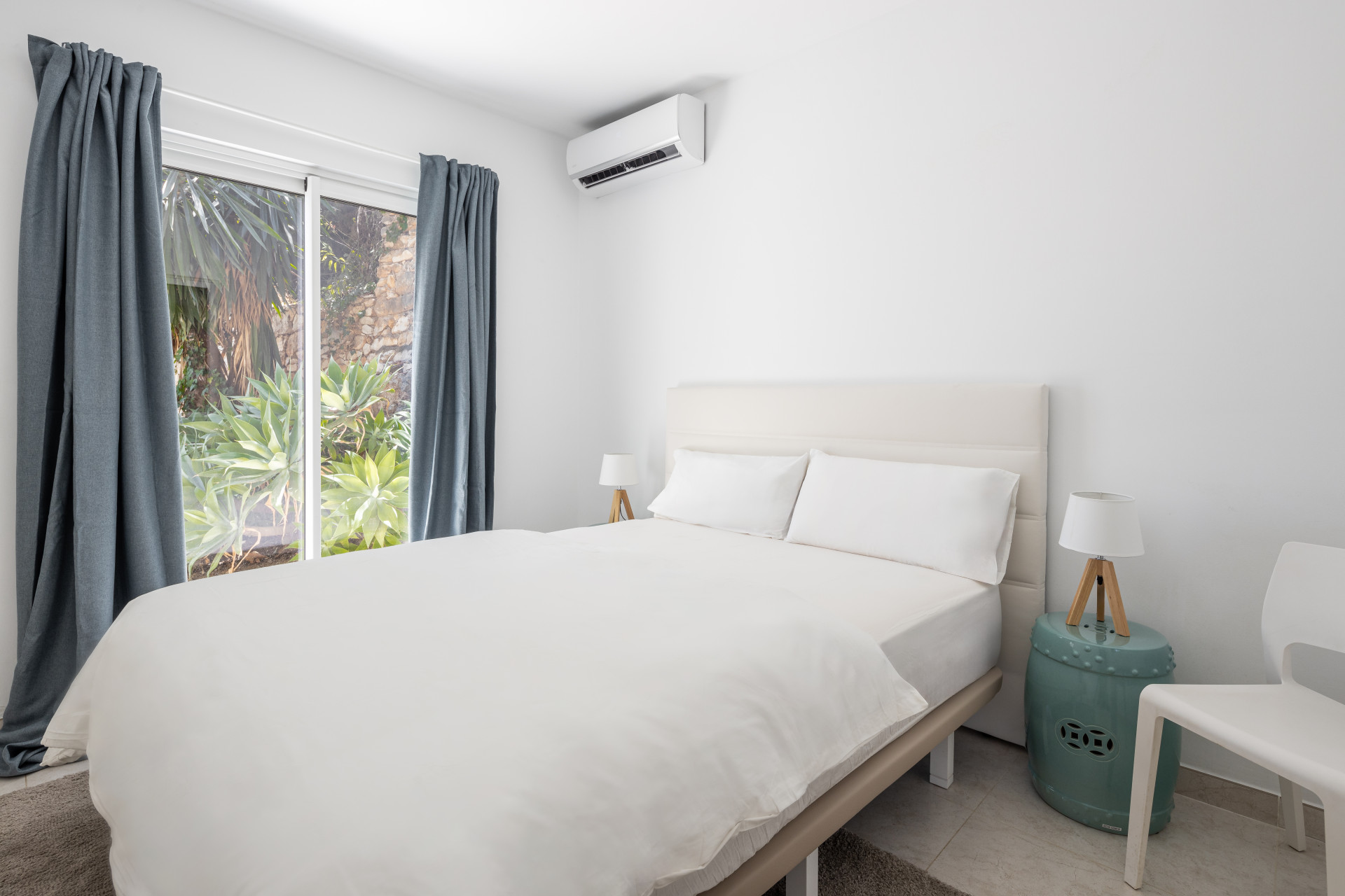 Bedroom with white bed, two bedside tables, air conditioning, and a sliding glass door to outside.