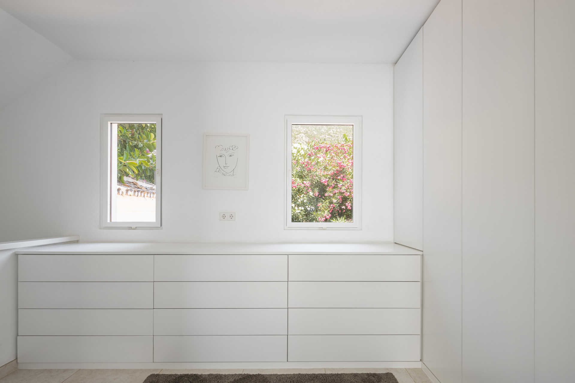 White dressing room with two windows showing greenery, long dresser, and integrated closet.