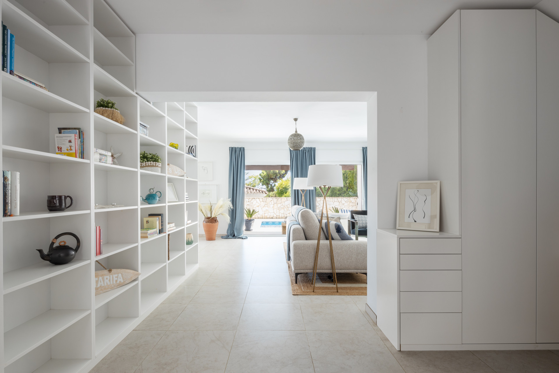 Hallway with built-in white shelving leading to a bright living room with outdoor pool view.