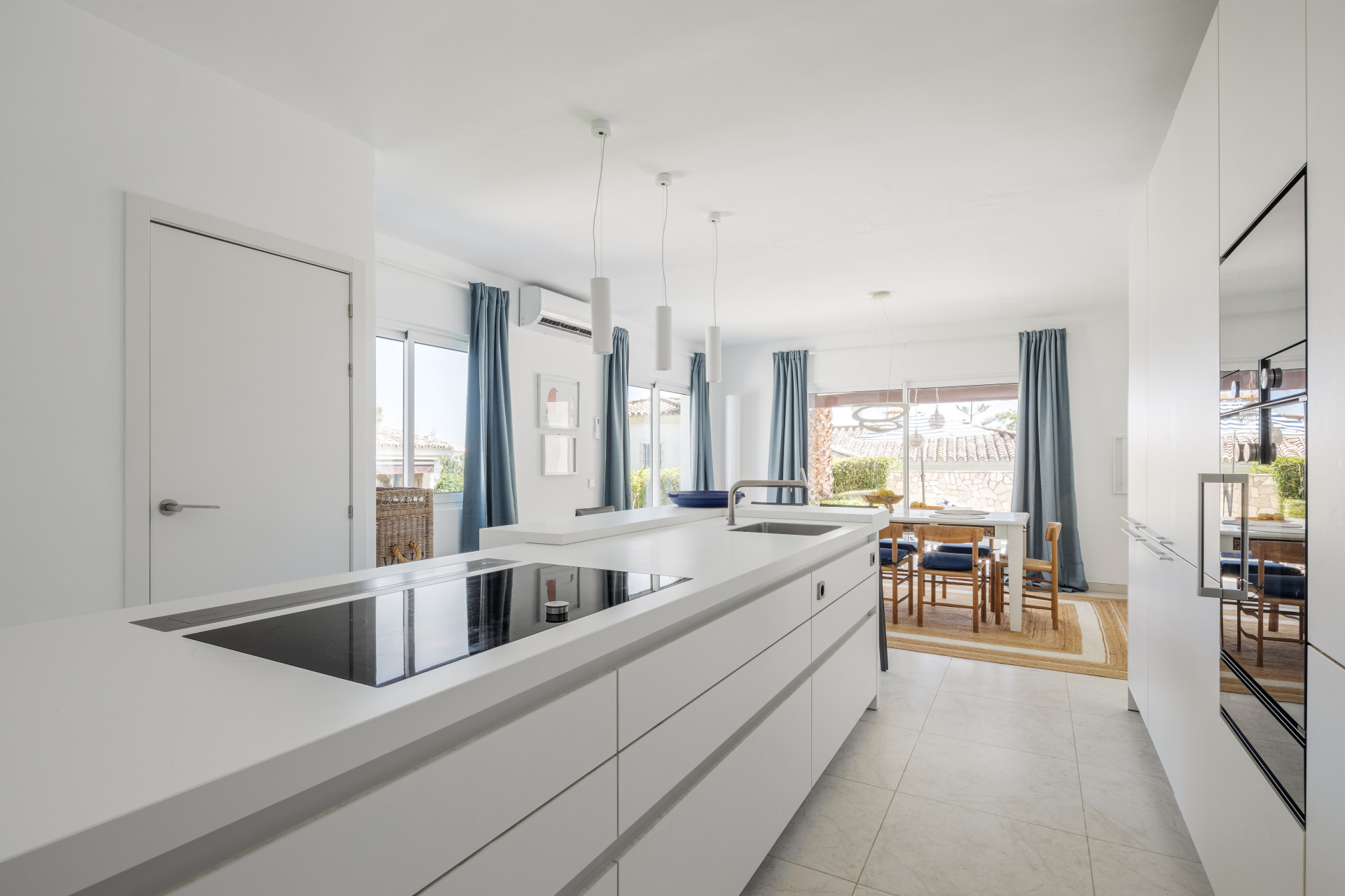 Modern kitchen with white cabinets, an induction cooktop, and a sink, looking towards a dining area.