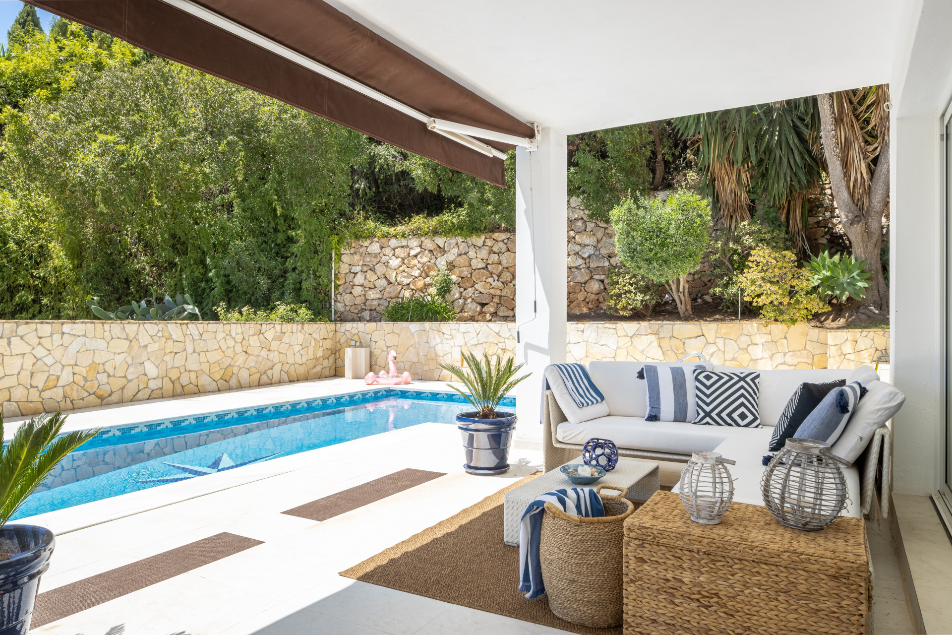 Covered patio with white sectional sofa, pillows, and a swimming pool in the foreground.