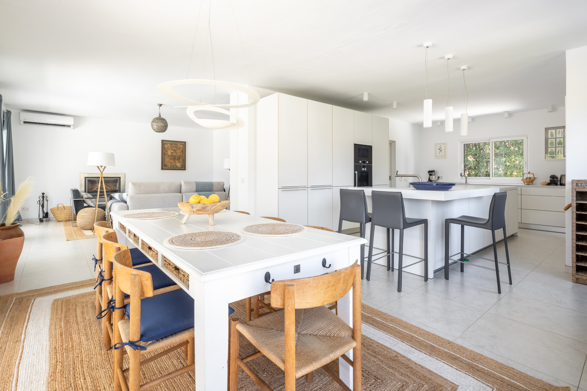 Open plan living area with a white dining table, wooden chairs, and a modern kitchen island with bar stools.