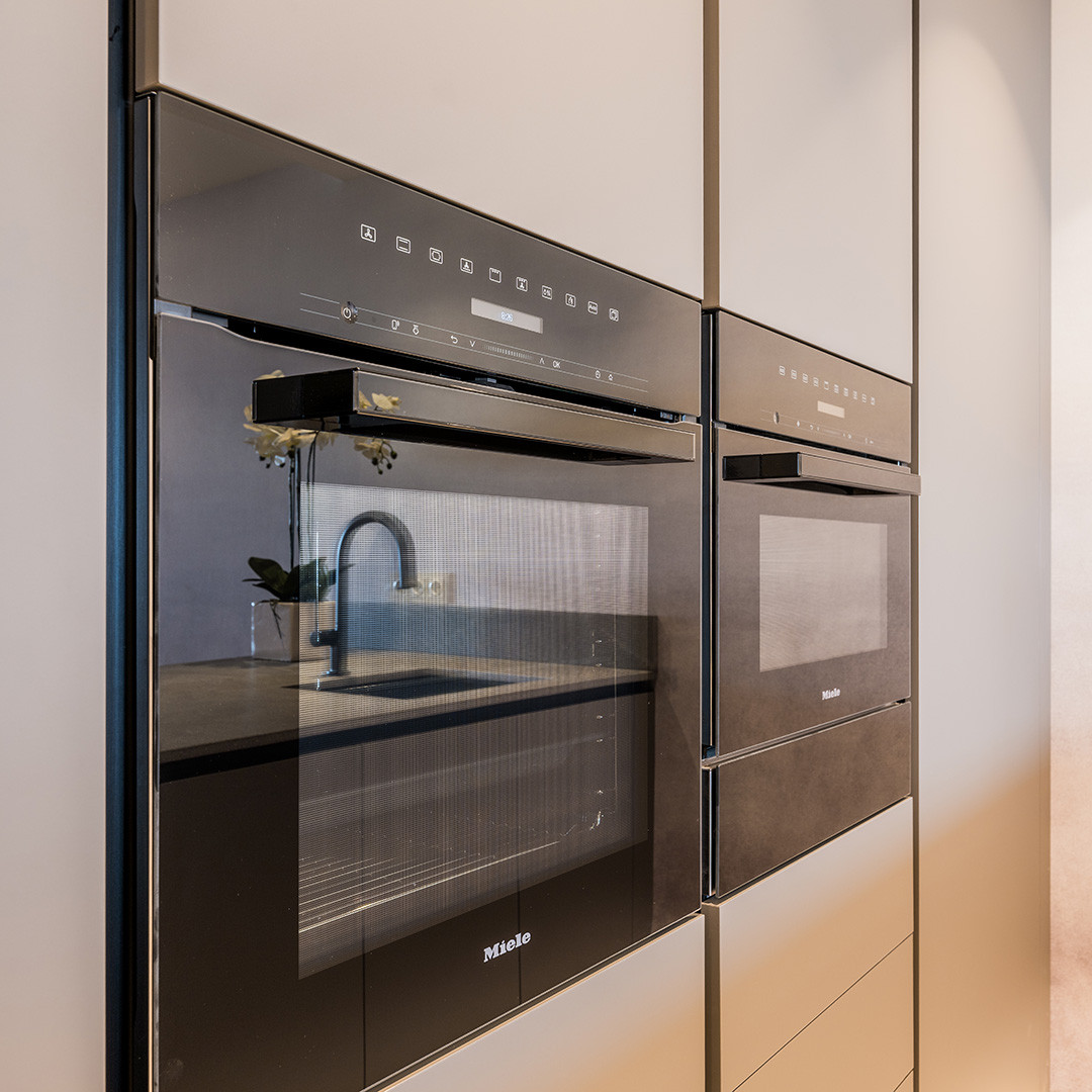 Close up of two Miele built-in ovens in a modern kitchen, reflecting the sink area.