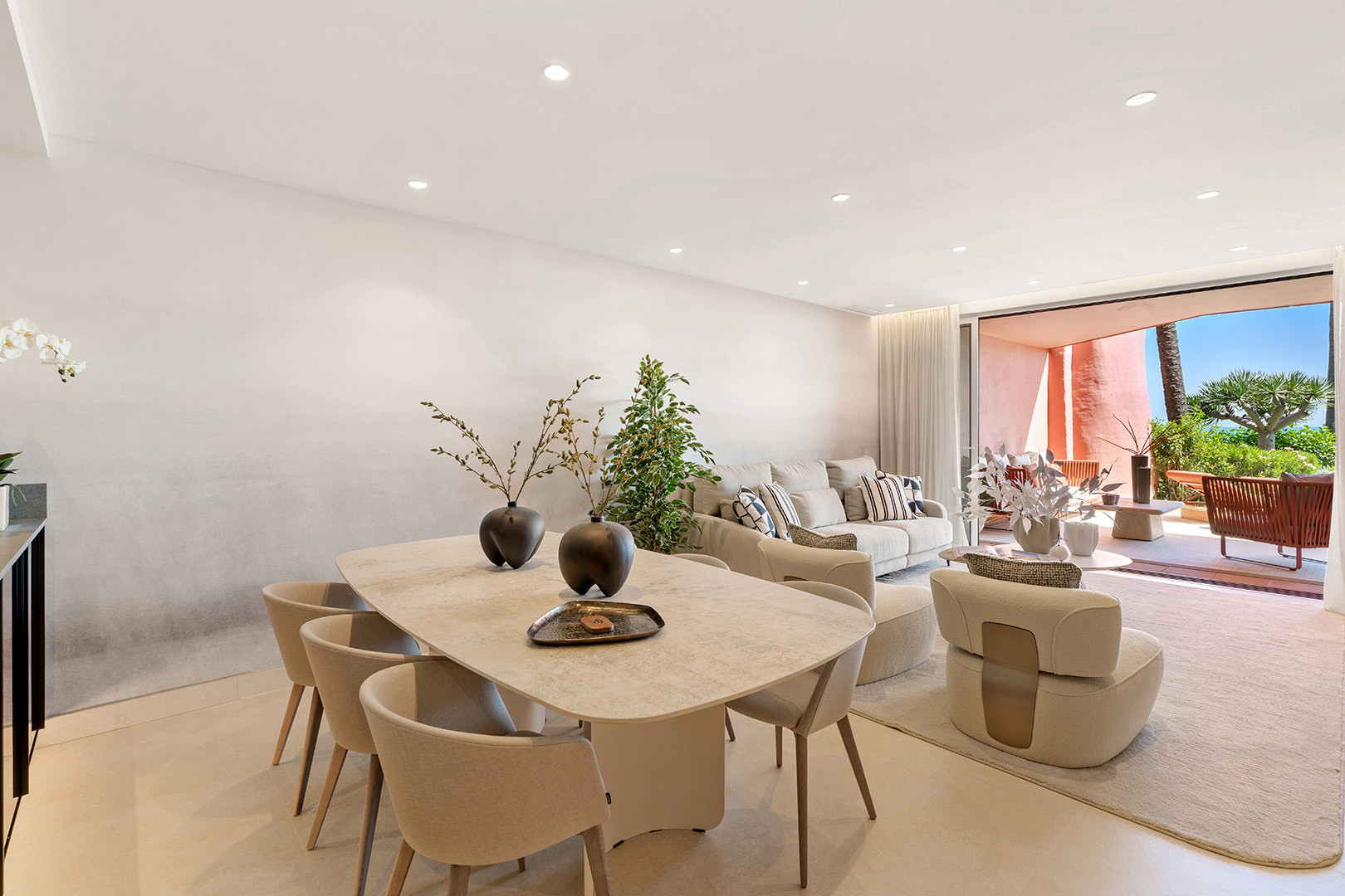 Dining table set with black vases and chairs, with a view into the living room and outdoor terrace.