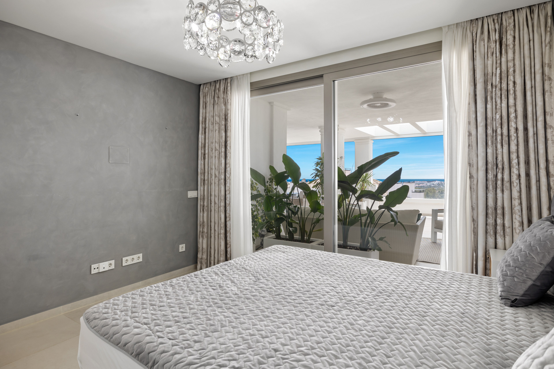 Bedroom view from the foot of the bed toward a large glass sliding door opening to a balcony with sea views.