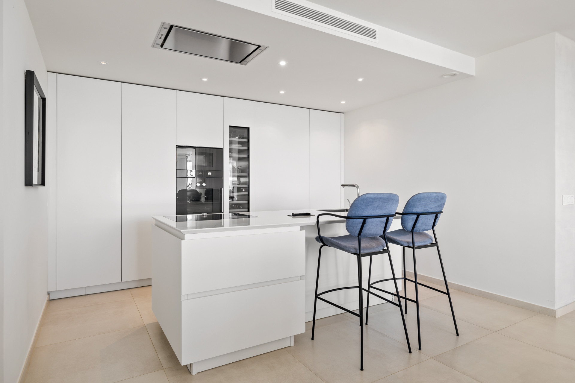 Modern white kitchen with integrated appliances and a central island with two blue bar stools.