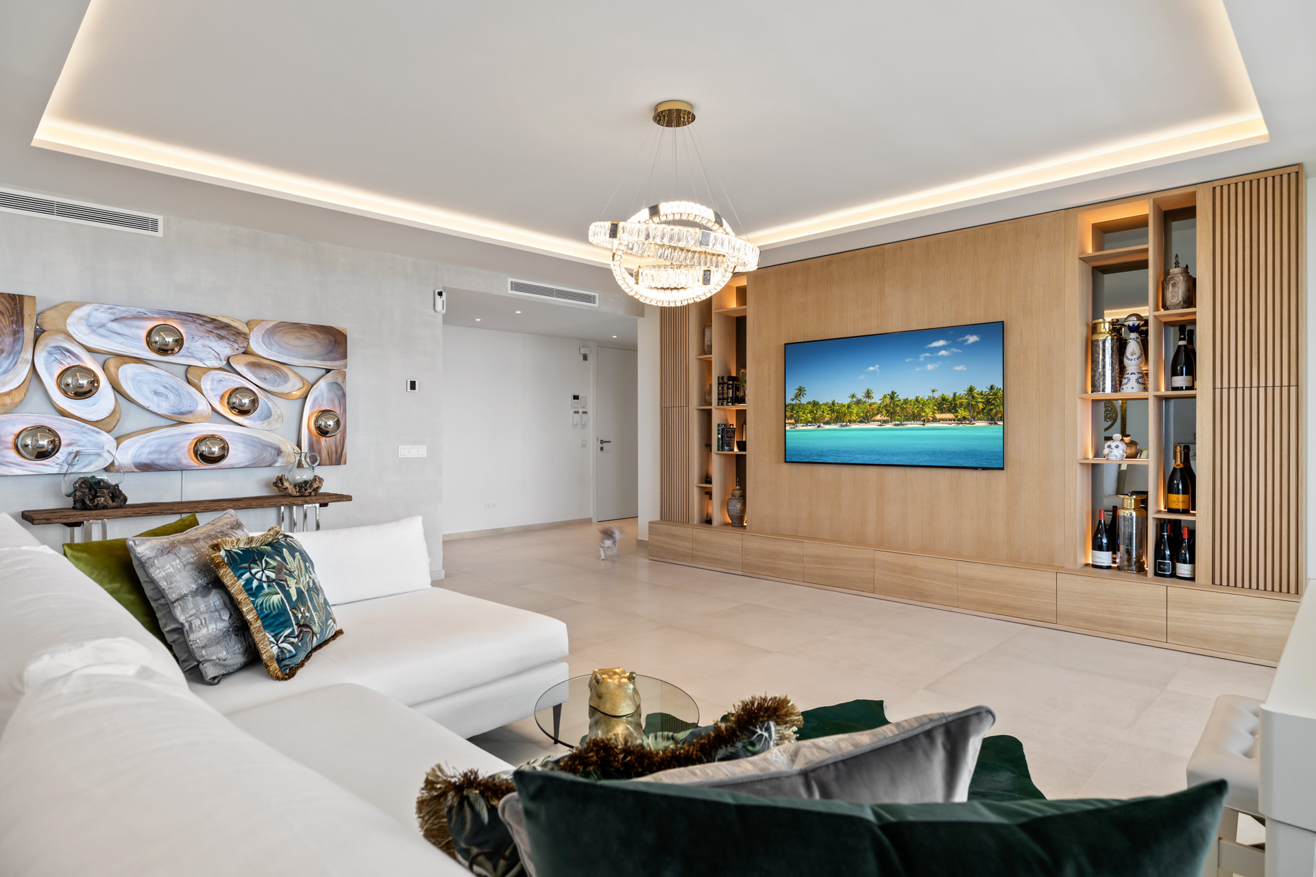 Bright living room with a white sectional sofa, wooden media wall, and sparkling chandelier.