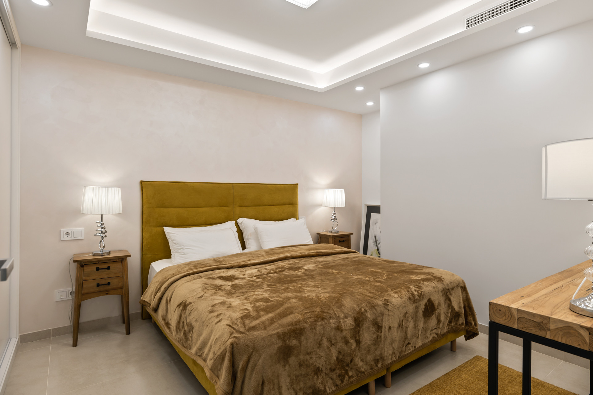 Bedroom with a yellow upholstered headboard, two wooden nightstands, and a golden bedspread.