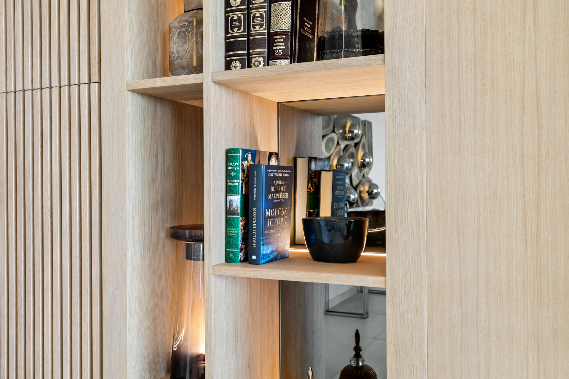 Close-up of a built-in wooden bookshelf with various books and decorative items, illuminated shelves.