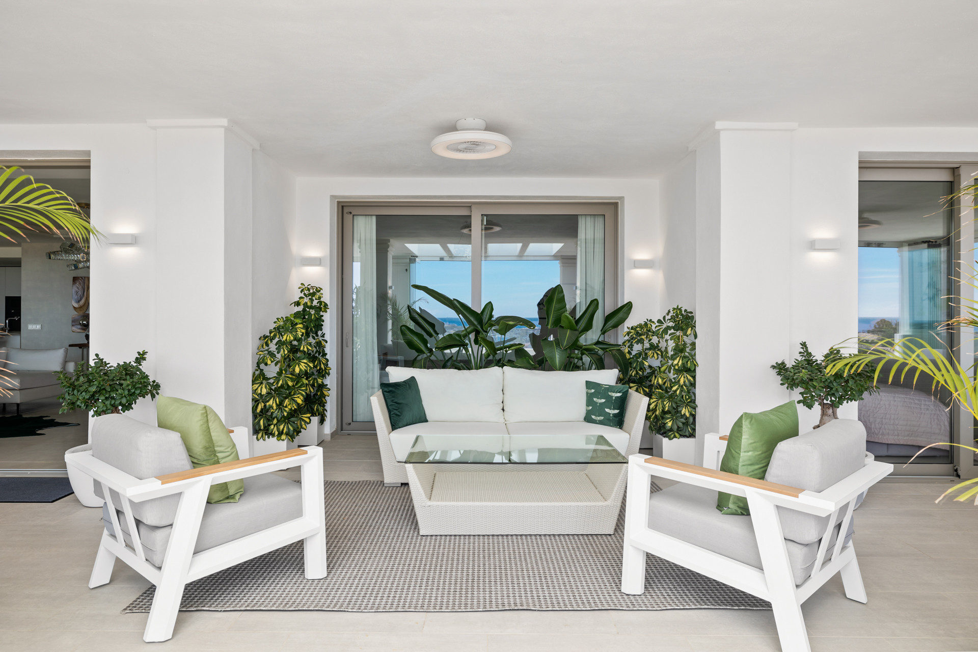 Outdoor seating with a white sofa, two armchairs, green cushions, and potted plants, overlooking the ocean.