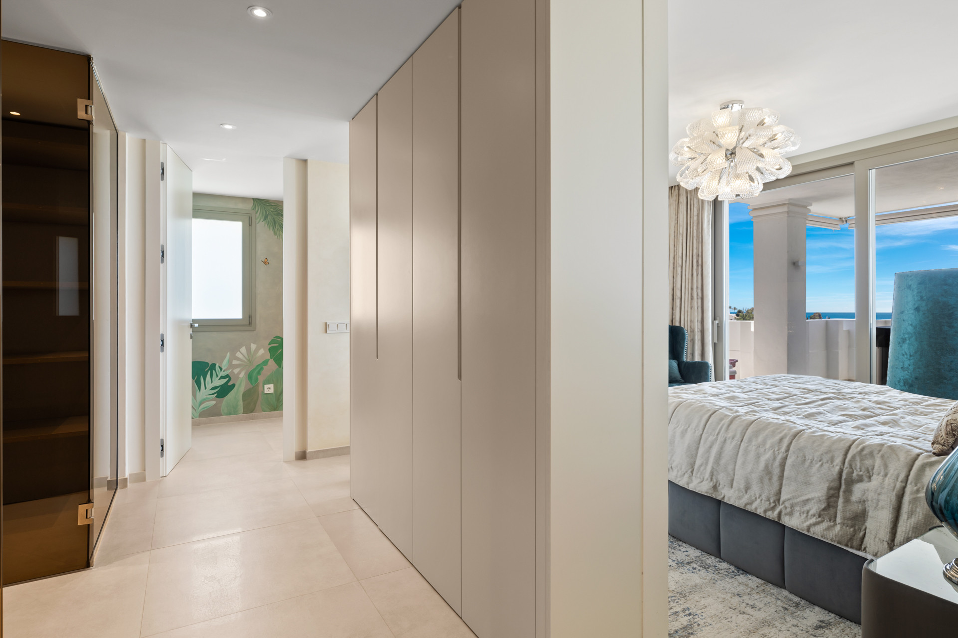 Hallway leading to a bedroom on the right and another room with botanical wallpaper ahead.