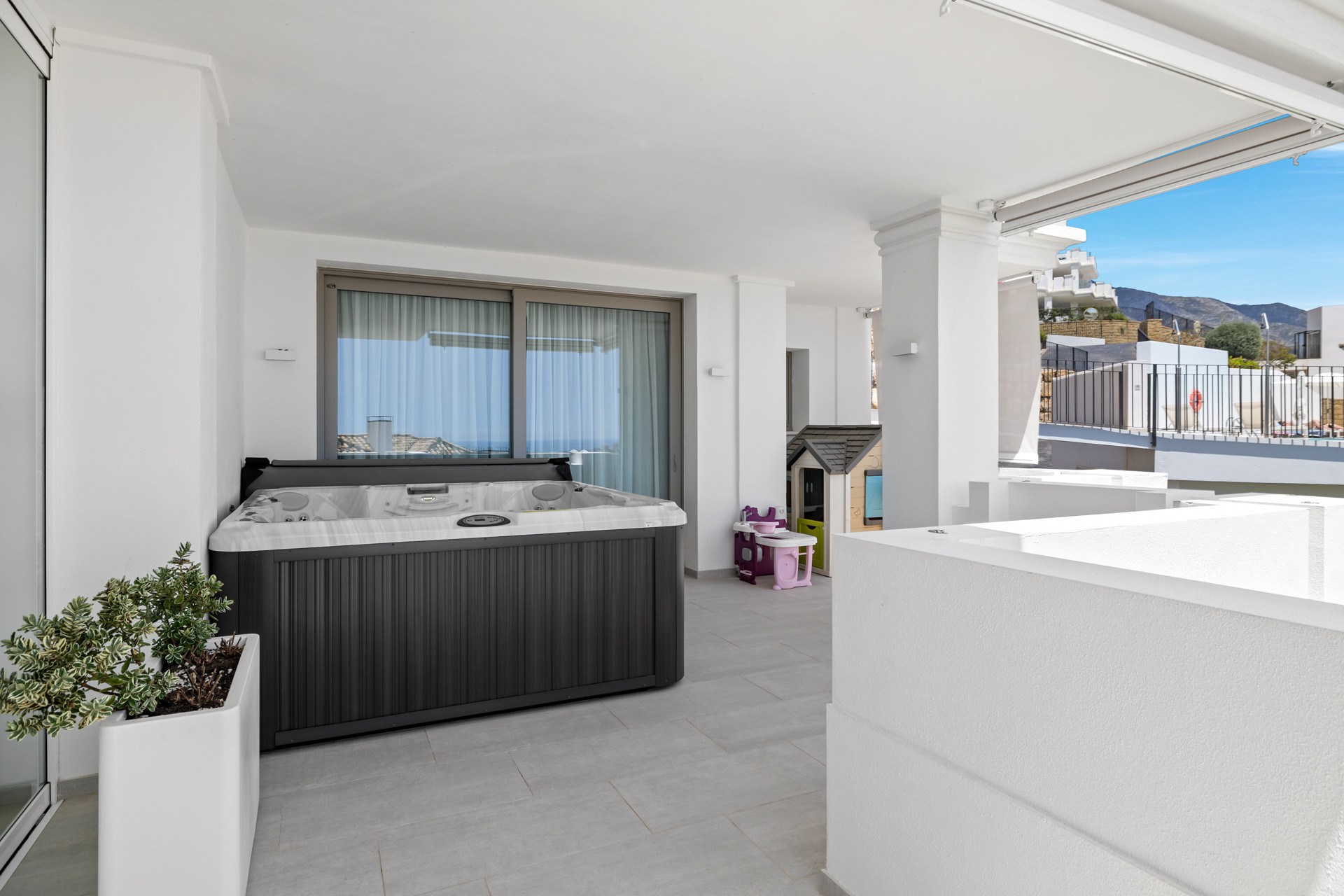 Outdoor patio with a dark grey hot tub, a small playhouse, and sliding glass doors.