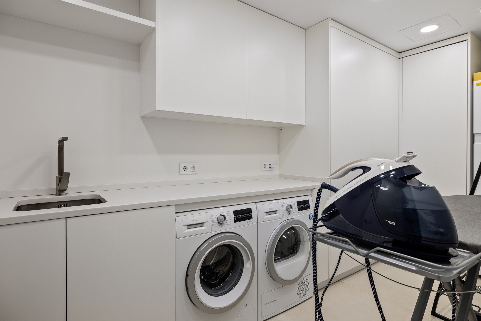 Laundry room with white cabinets, a sink, a washing machine, a dryer, and an ironing station.