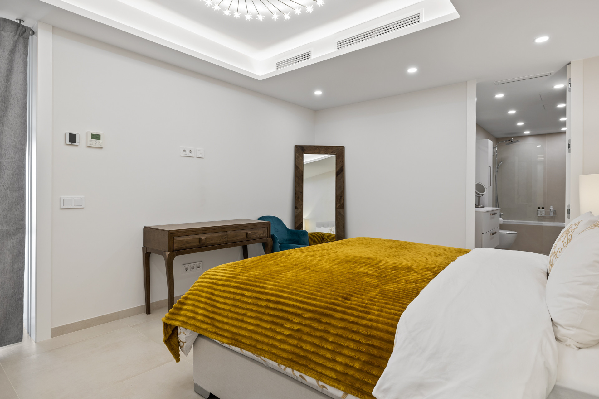 Bedroom with a bed with yellow comforter, wooden desk, full-length mirror, and visible bathroom.