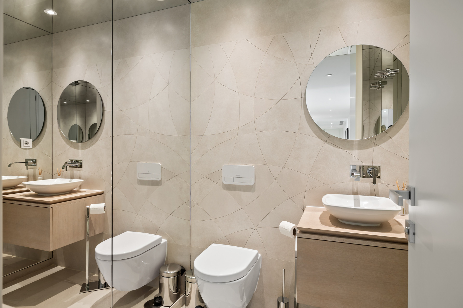 Bathroom with light tiled walls, two floating vanities, two vessel sinks, and two wall mounted toilets.