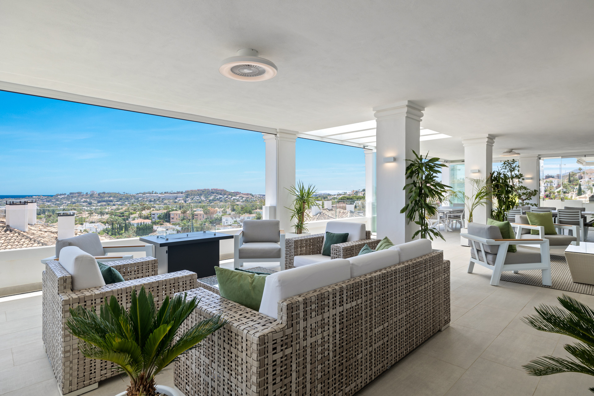 Expansive covered outdoor living space with multiple seating areas, a fire pit, and extensive city and ocean views.