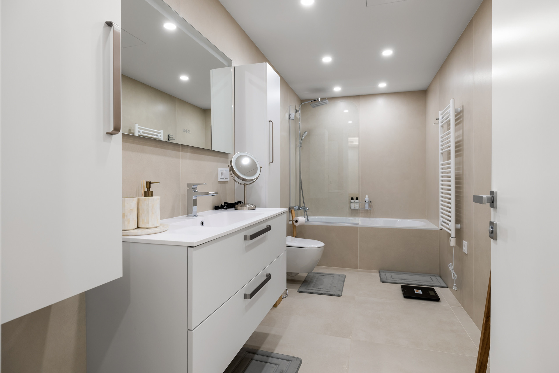 Modern bathroom with white vanity, large mirror, toilet, and tiled shower tub combo.