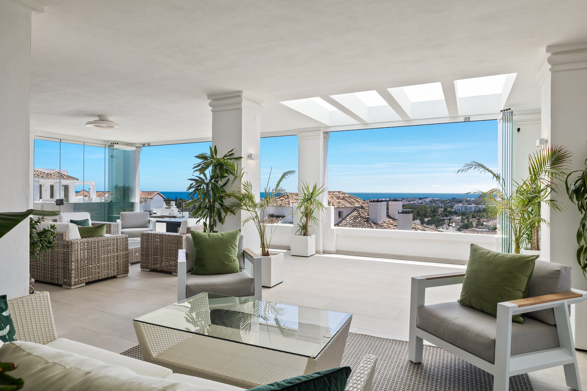 Spacious covered outdoor lounge area with wicker furniture, green cushions, and a glass coffee table.