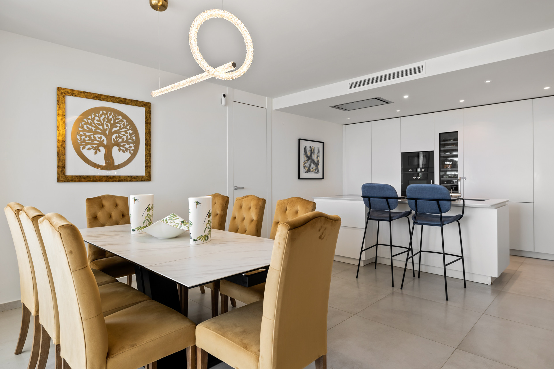 Open concept dining area featuring a long white table, gold chairs, and a visible modern kitchen island.