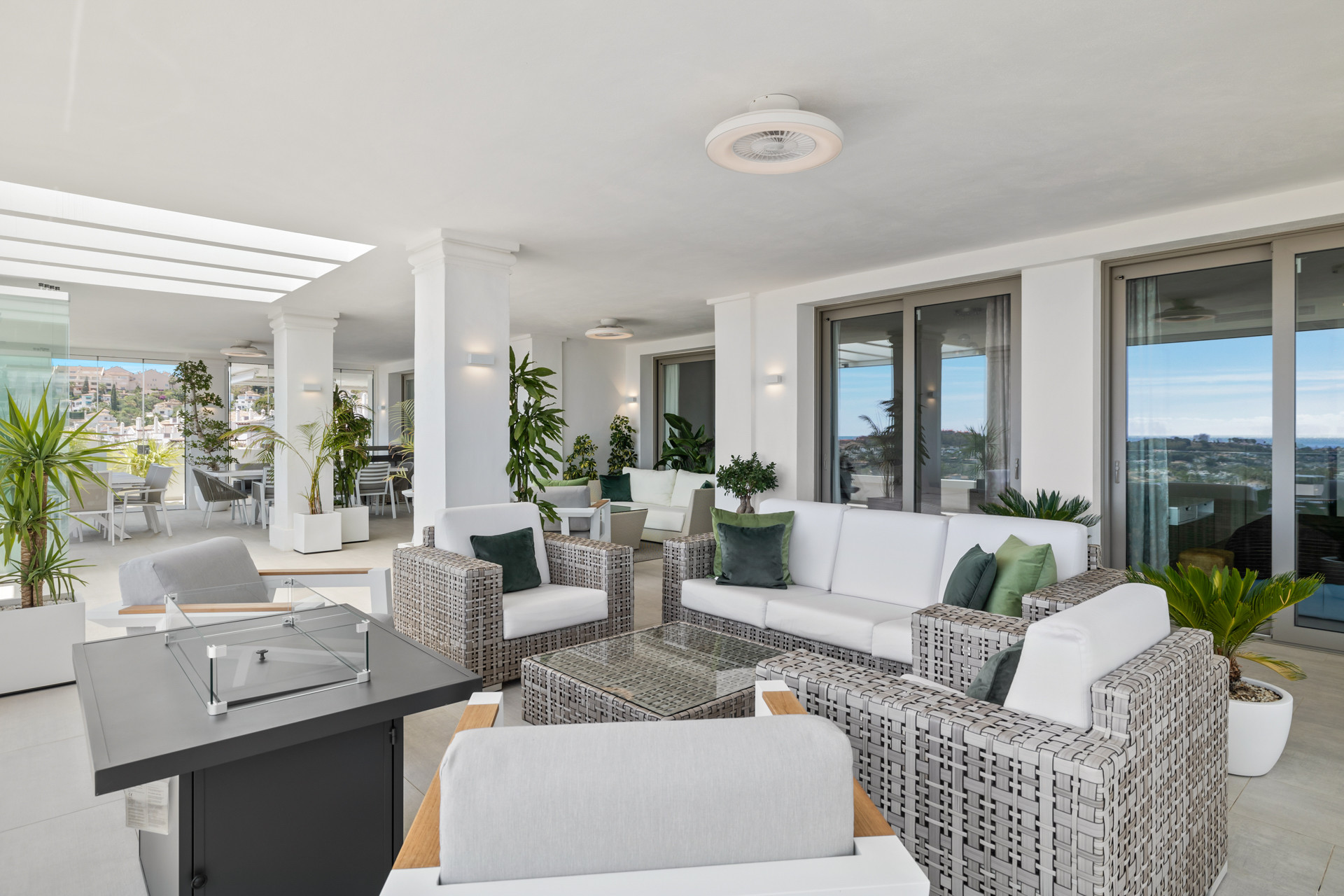Outdoor lounge with white wicker sofas and green cushions, glass coffee table, and plants.