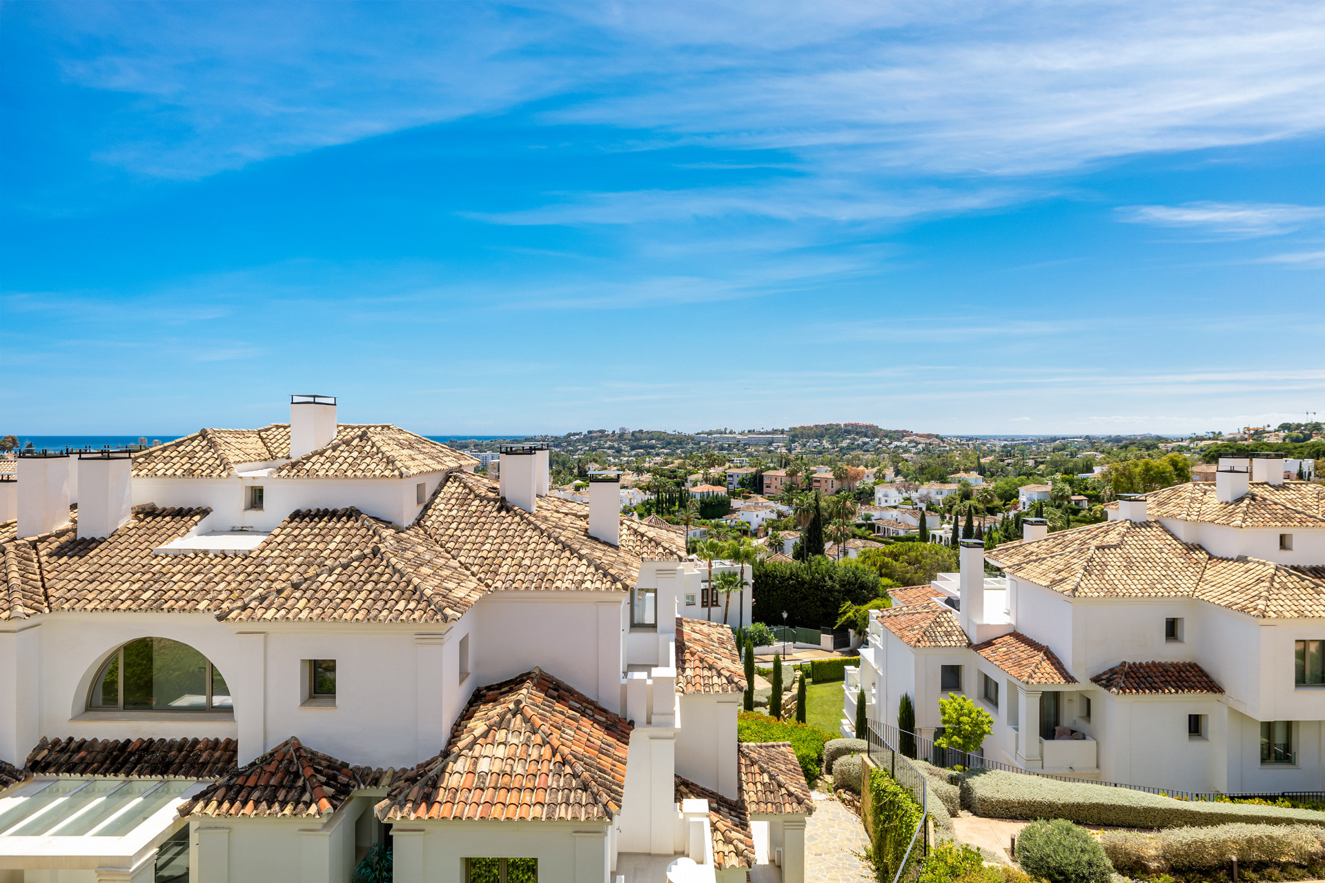 View over white buildings with terracotta roofs, revealing a townscape and distant ocean.