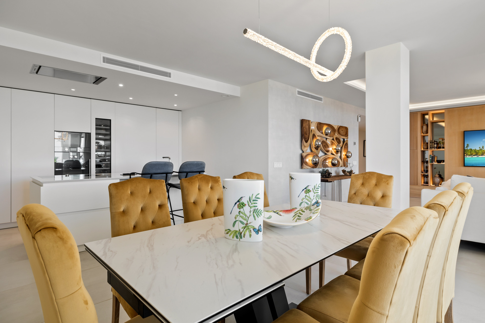 Open plan dining area with gold velvet chairs and a white marble table next to a contemporary kitchen.
