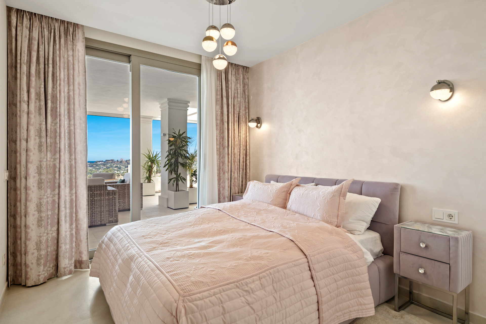 Bedroom with pink bedding, decorative ceiling lights, and sliding glass doors opening to a balcony.