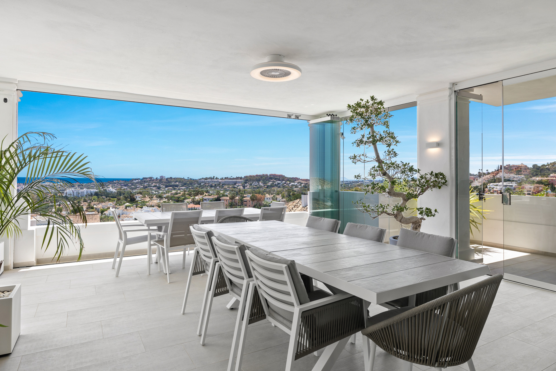 Outdoor dining area with two large tables and chairs, offering panoramic ocean and city views.