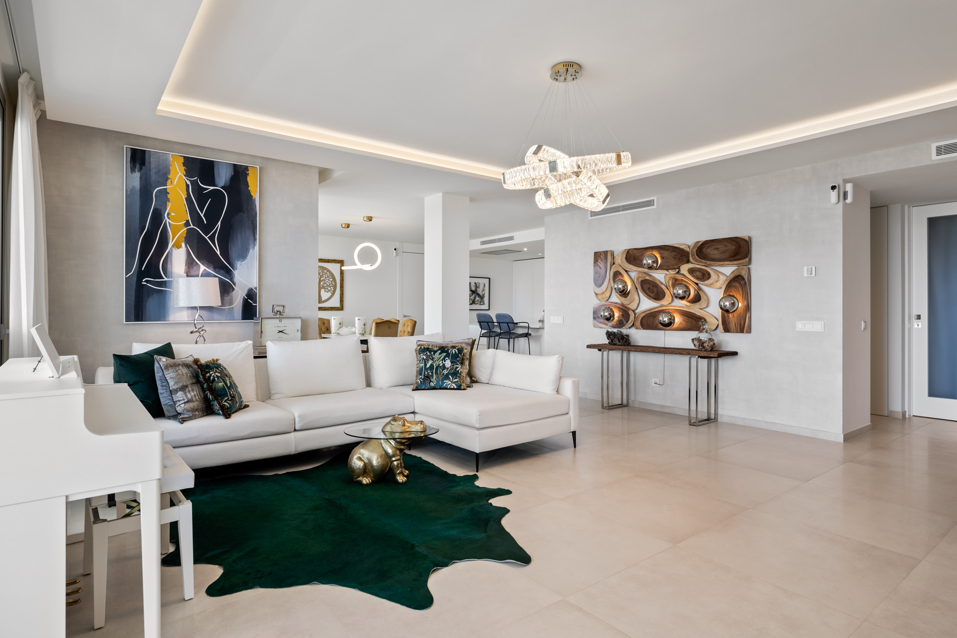 Modern living room with a large white sofa, dark green rug, artwork, and elegant chandelier.