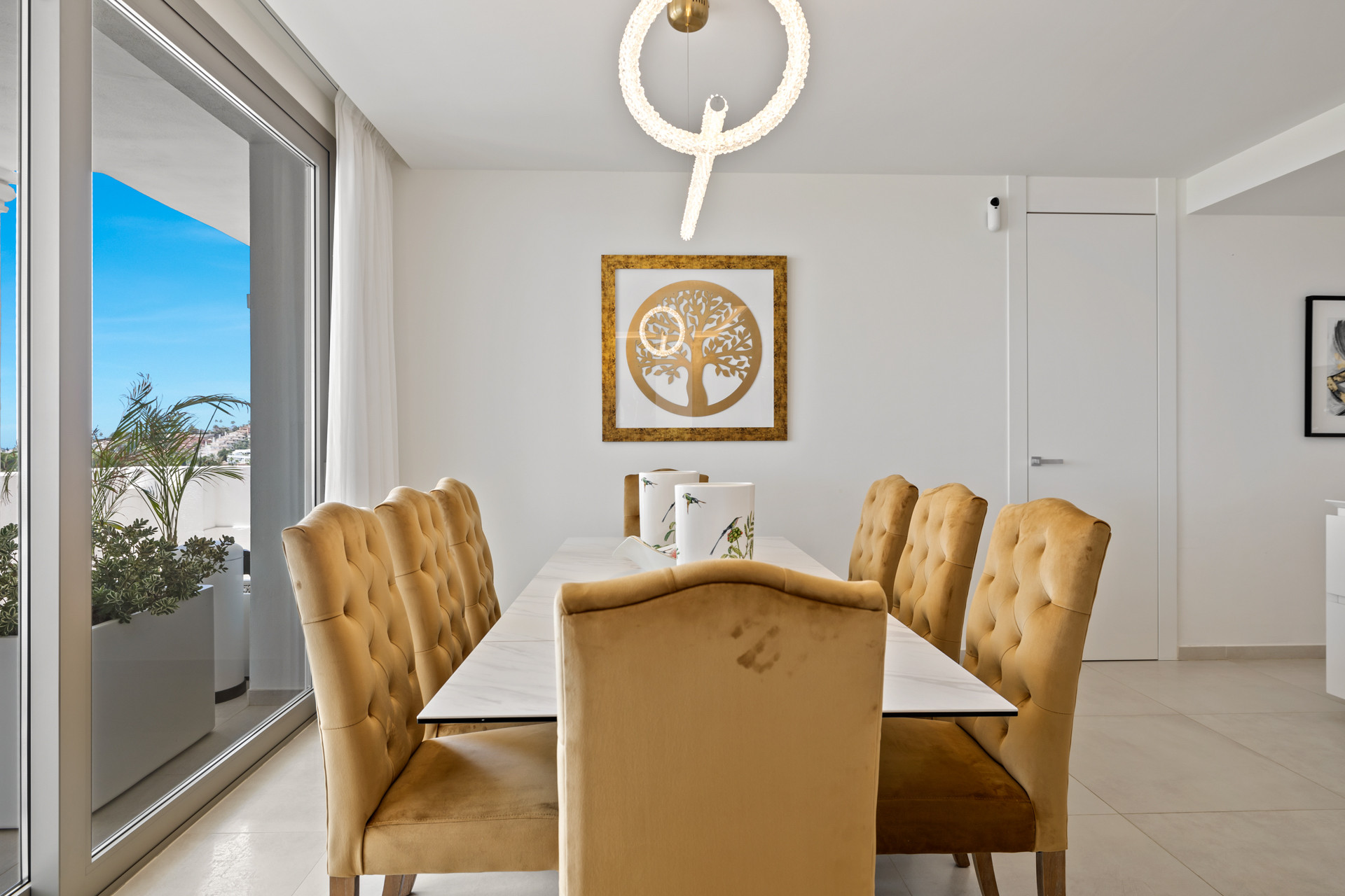 Dining room with gold velvet chairs, a white table, and a large sliding glass door to an outdoor area.