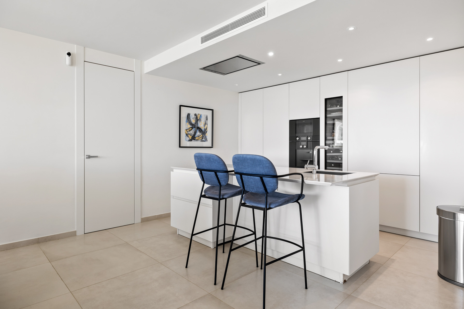 Modern kitchen with white cabinetry, a central island, two blue bar stools, and integrated appliances.