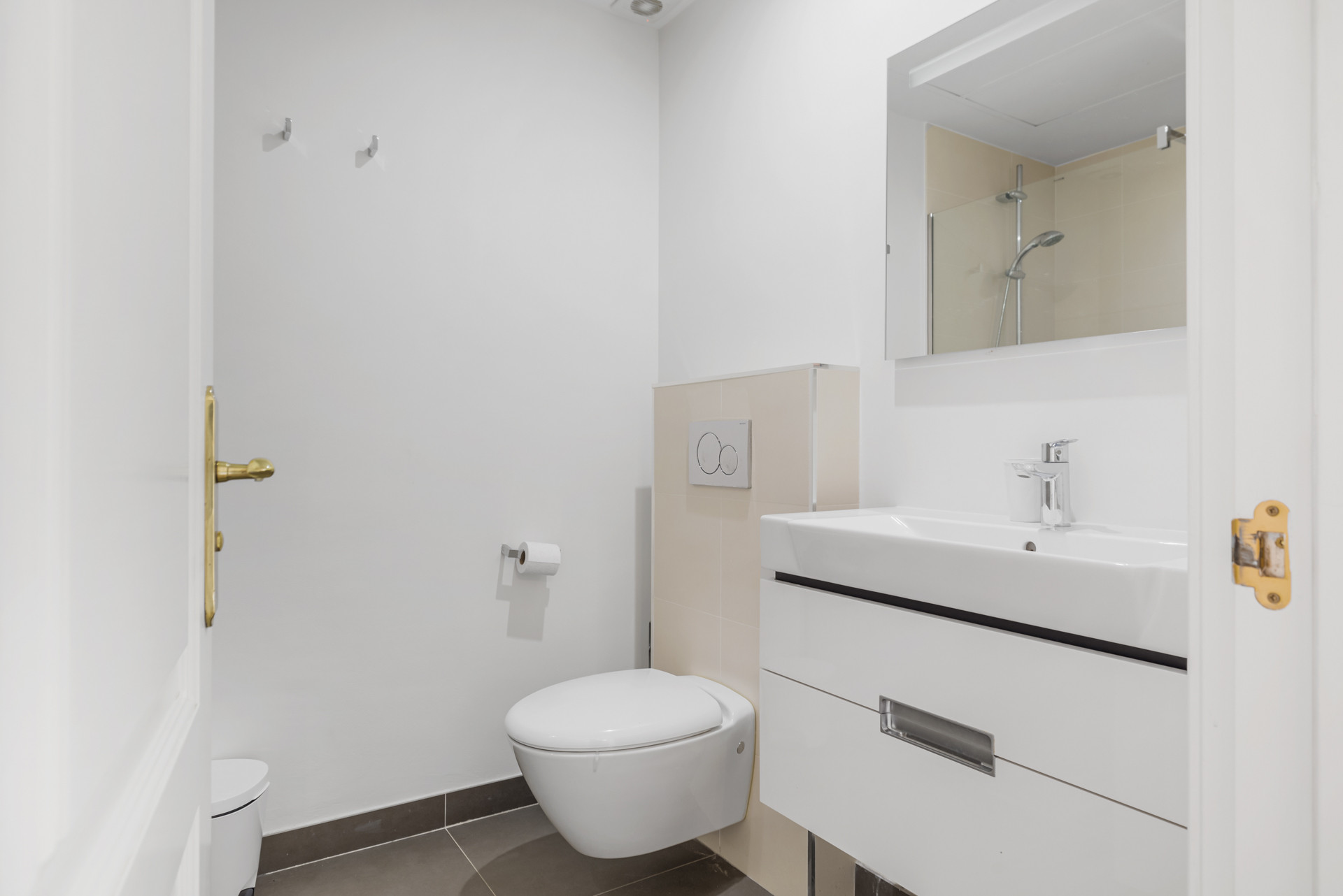 Bathroom with a white toilet, modern vanity, mirror, shower, and light beige tiled accents.