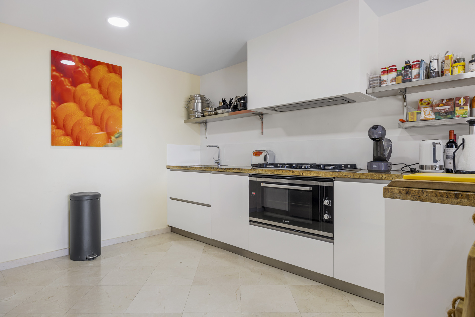 Modern kitchen with white cabinetry, built-in oven, gas hob, and an orange fruit art piece.