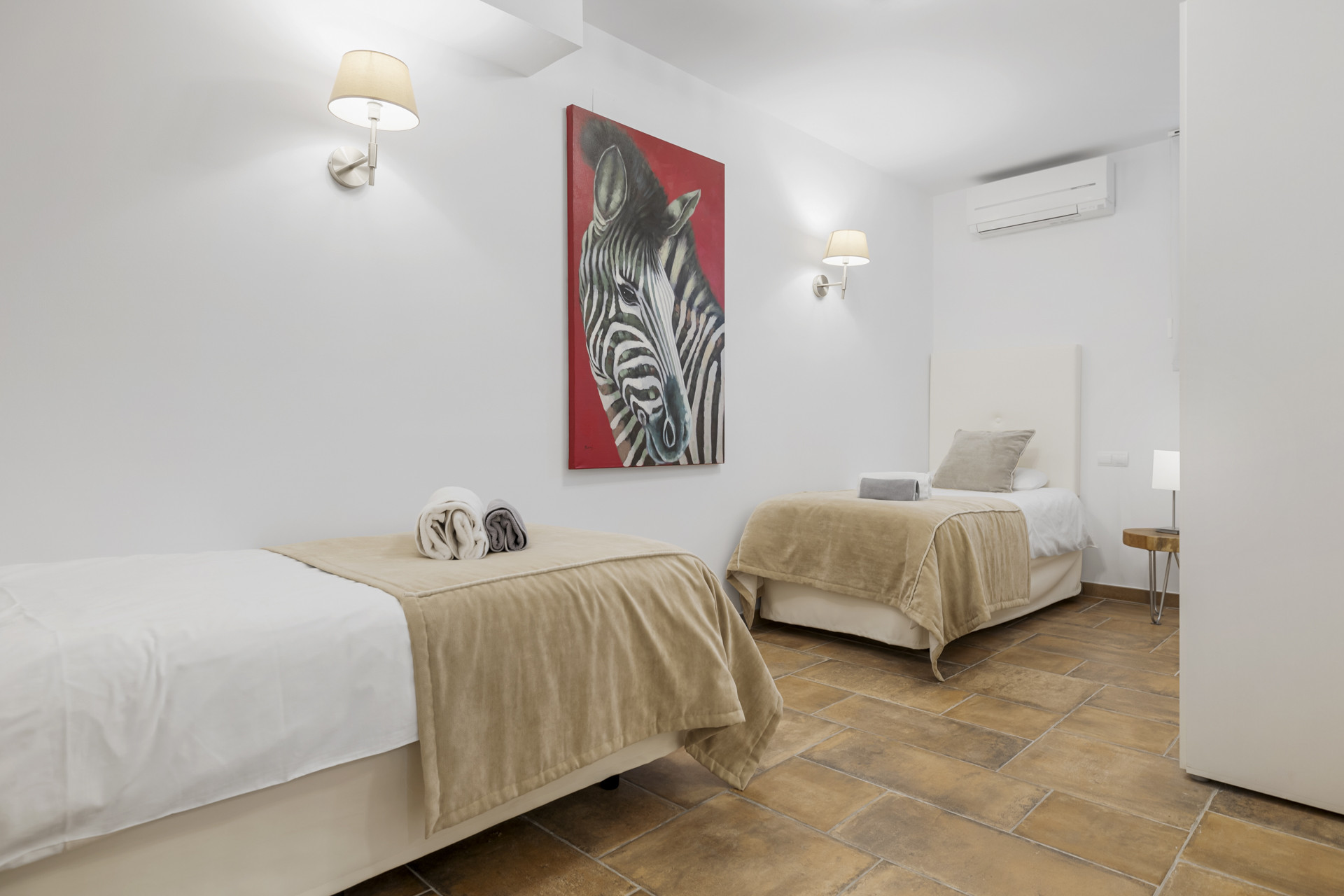 Bedroom with two single beds, tiled floor, white walls, and a zebra painting on a red background.