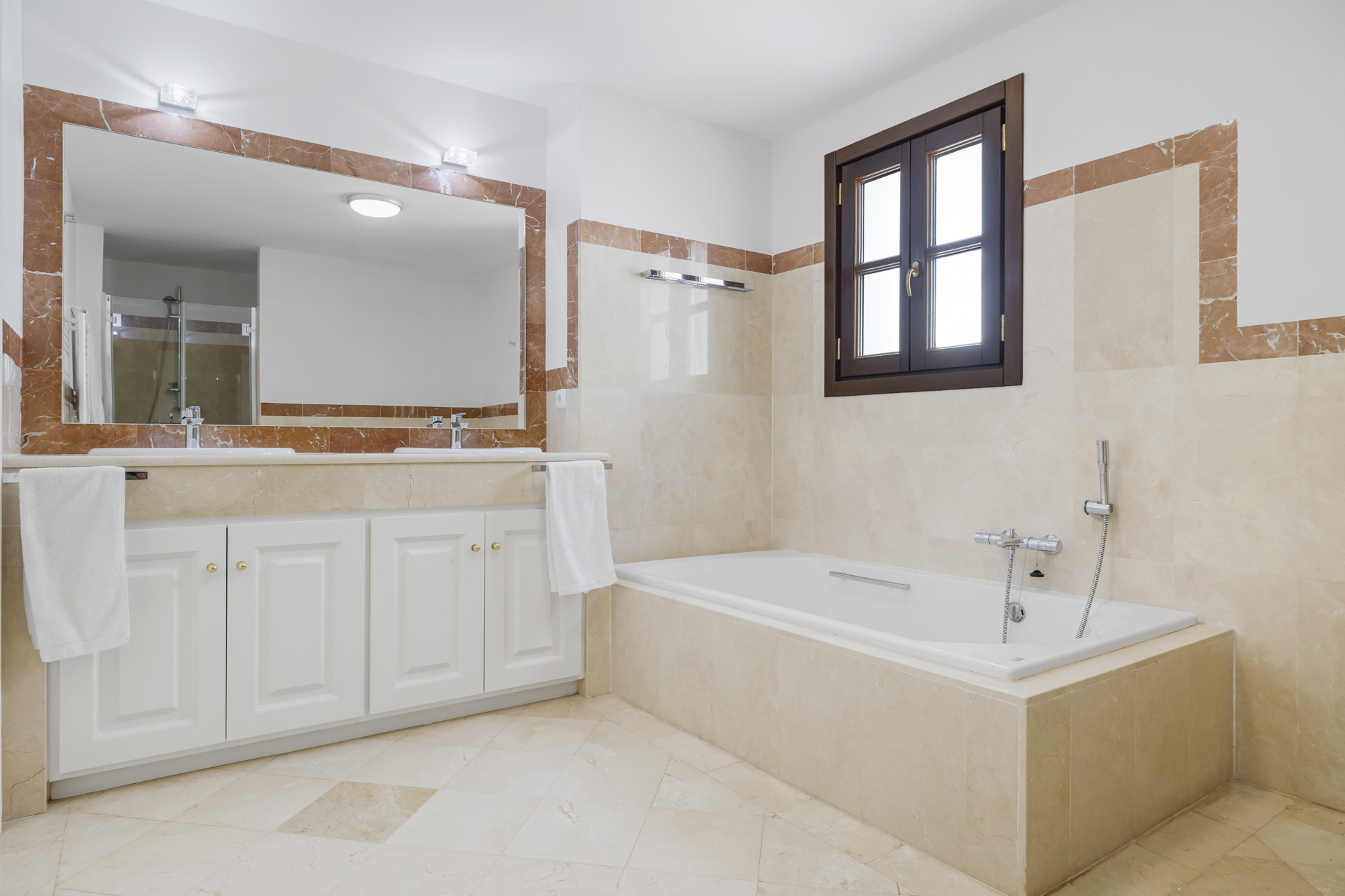 Bathroom with a double vanity, large mirror, and a built-in bathtub under a window.