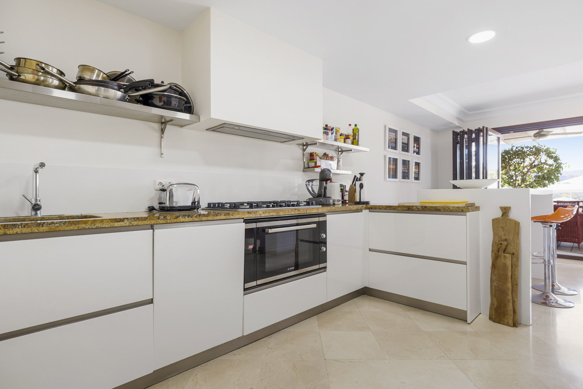 Modern white kitchen with granite countertops, stainless steel appliances, and a view to the outside.