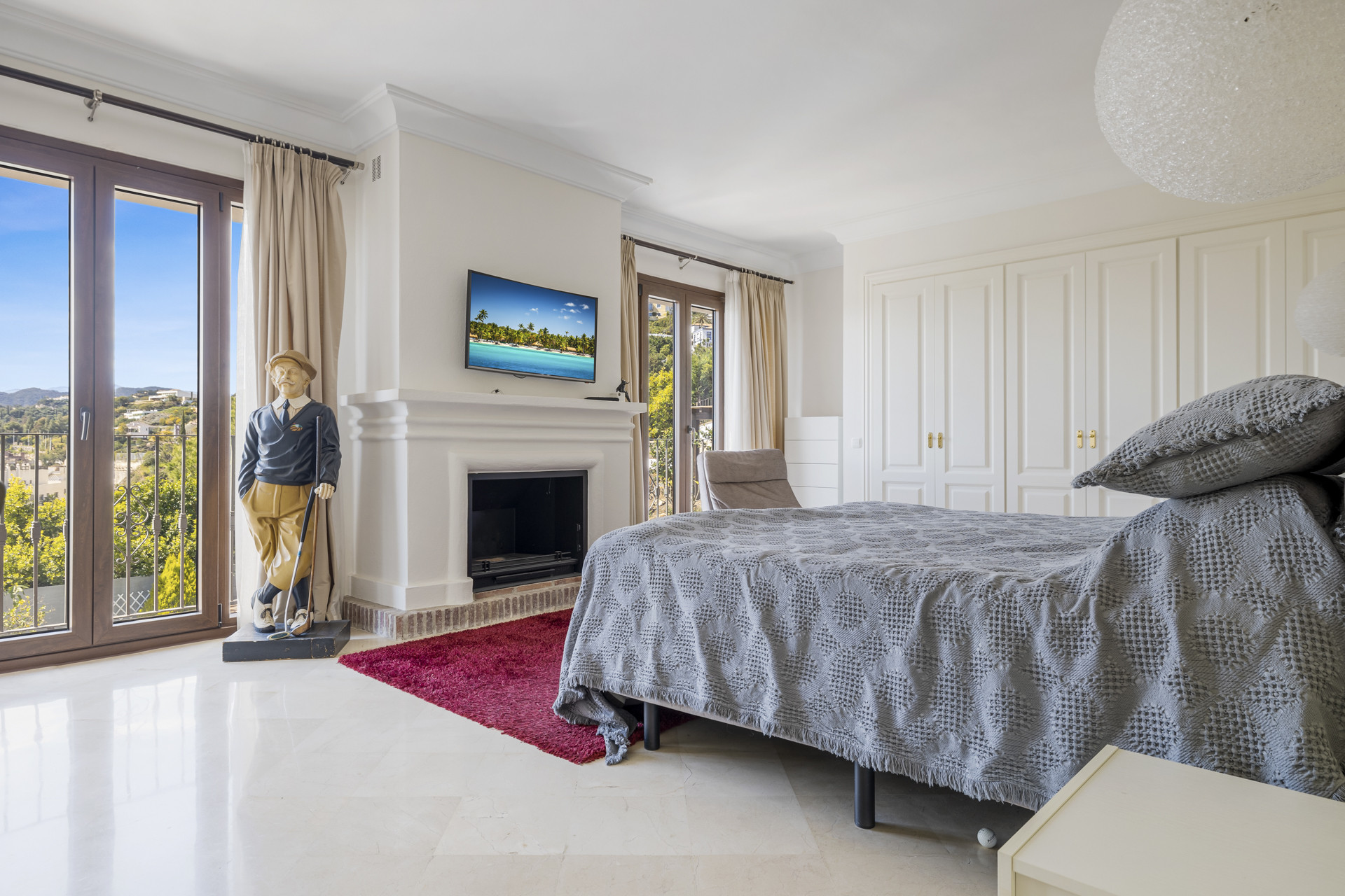 Bedroom with a large bed, fireplace, wall-mounted TV, and glass doors to a balcony view.