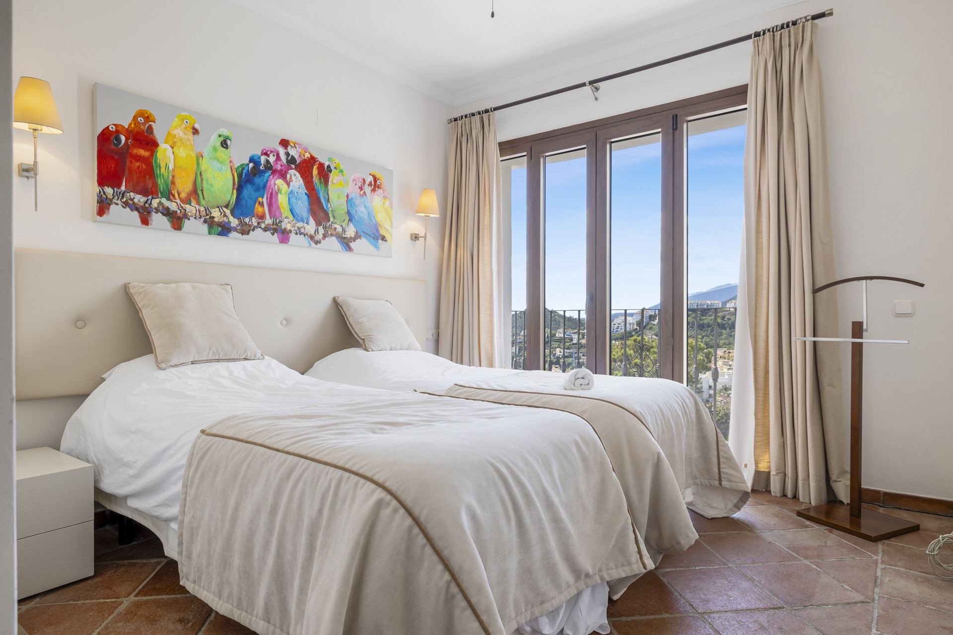 Bedroom with two twin beds, colorful parrot artwork, and glass doors opening to a balcony view.