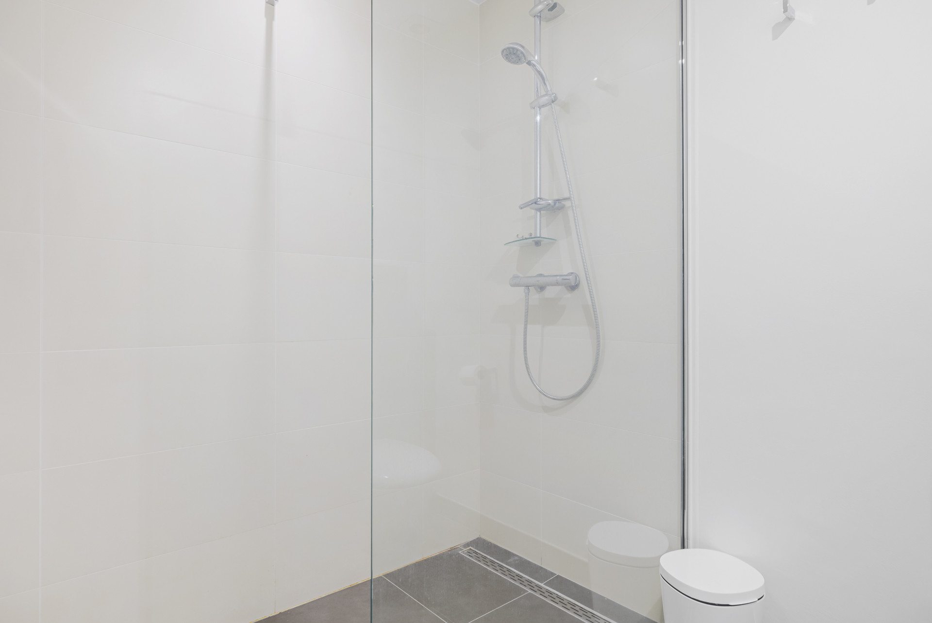 White tiled shower with a glass enclosure, gray floor, and a minimalist design.