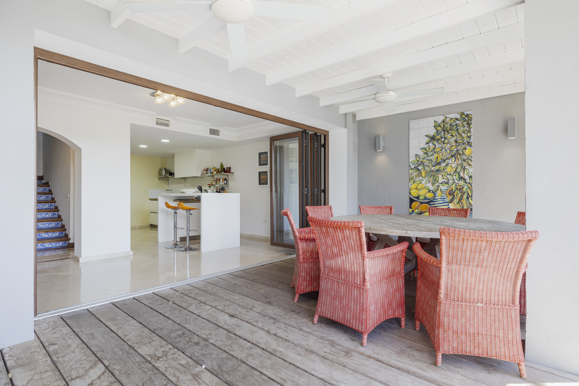 Outdoor dining area with a circular table and coral-colored chairs, overlooking an open kitchen.