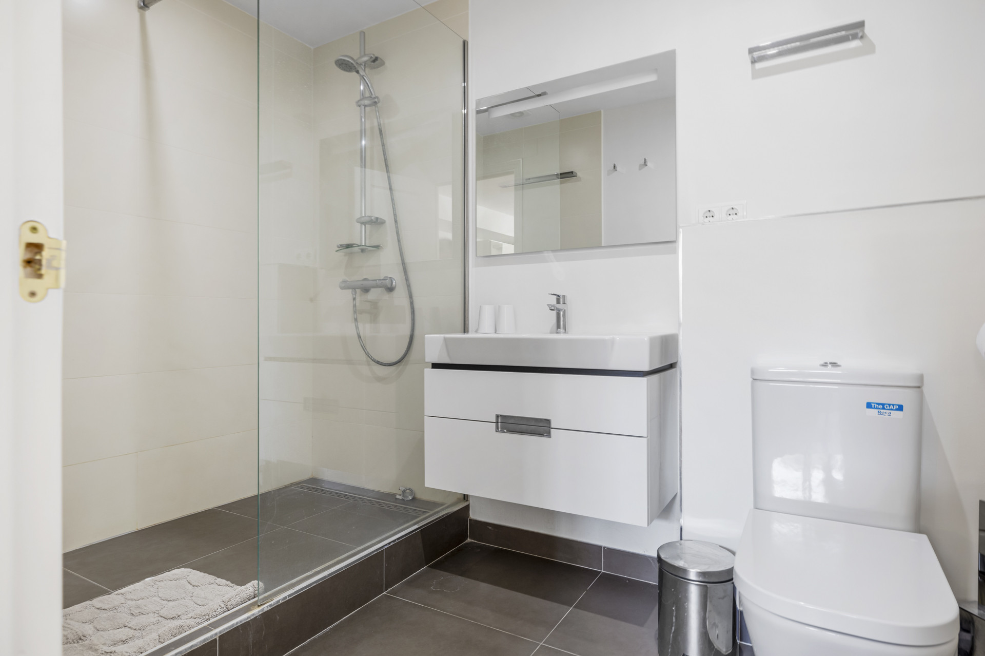 Bathroom with a glass shower, floating vanity, mirror, and toilet with a white lid.