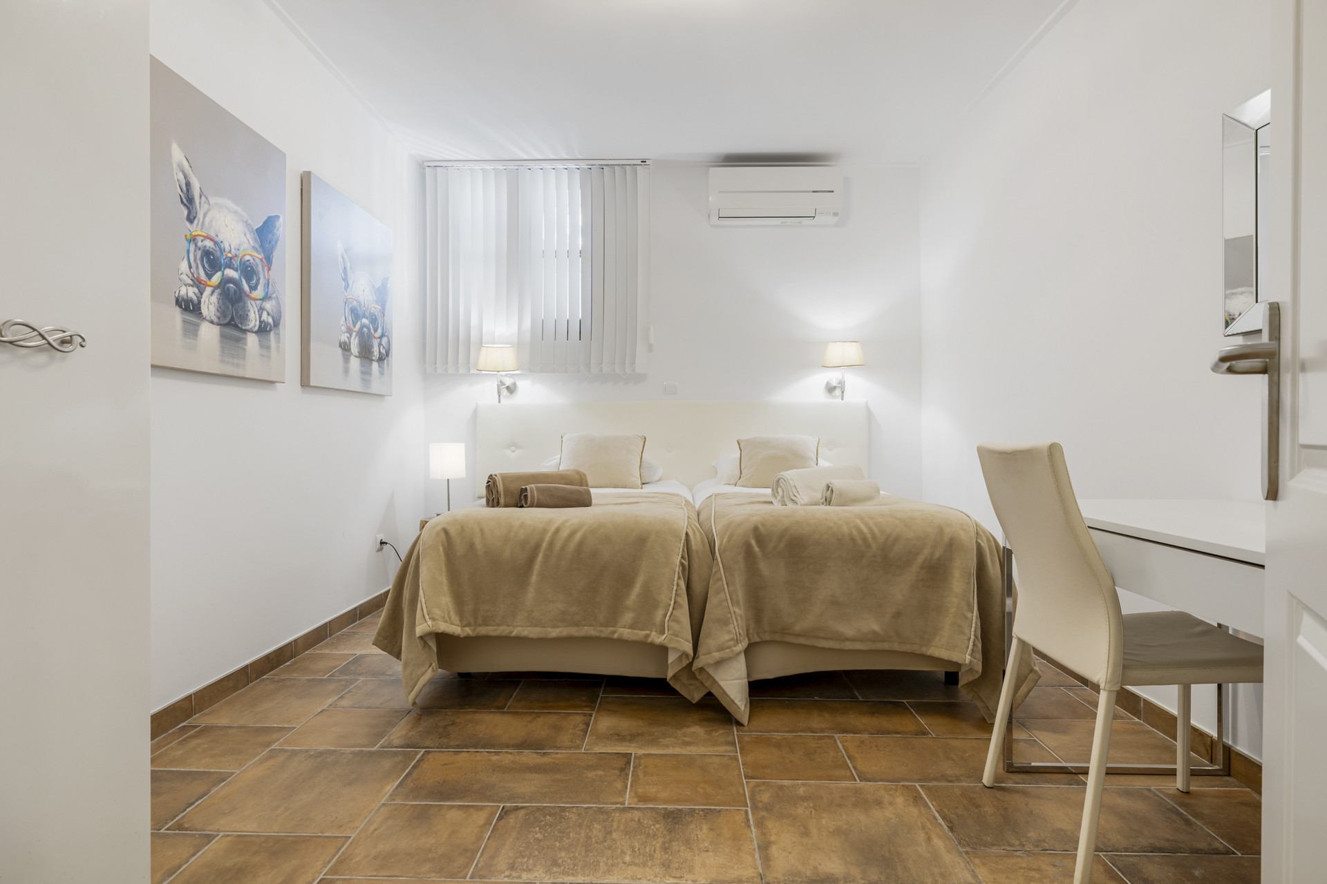 Bedroom with two single beds, white headboard, white walls, and two colorful bulldog paintings.