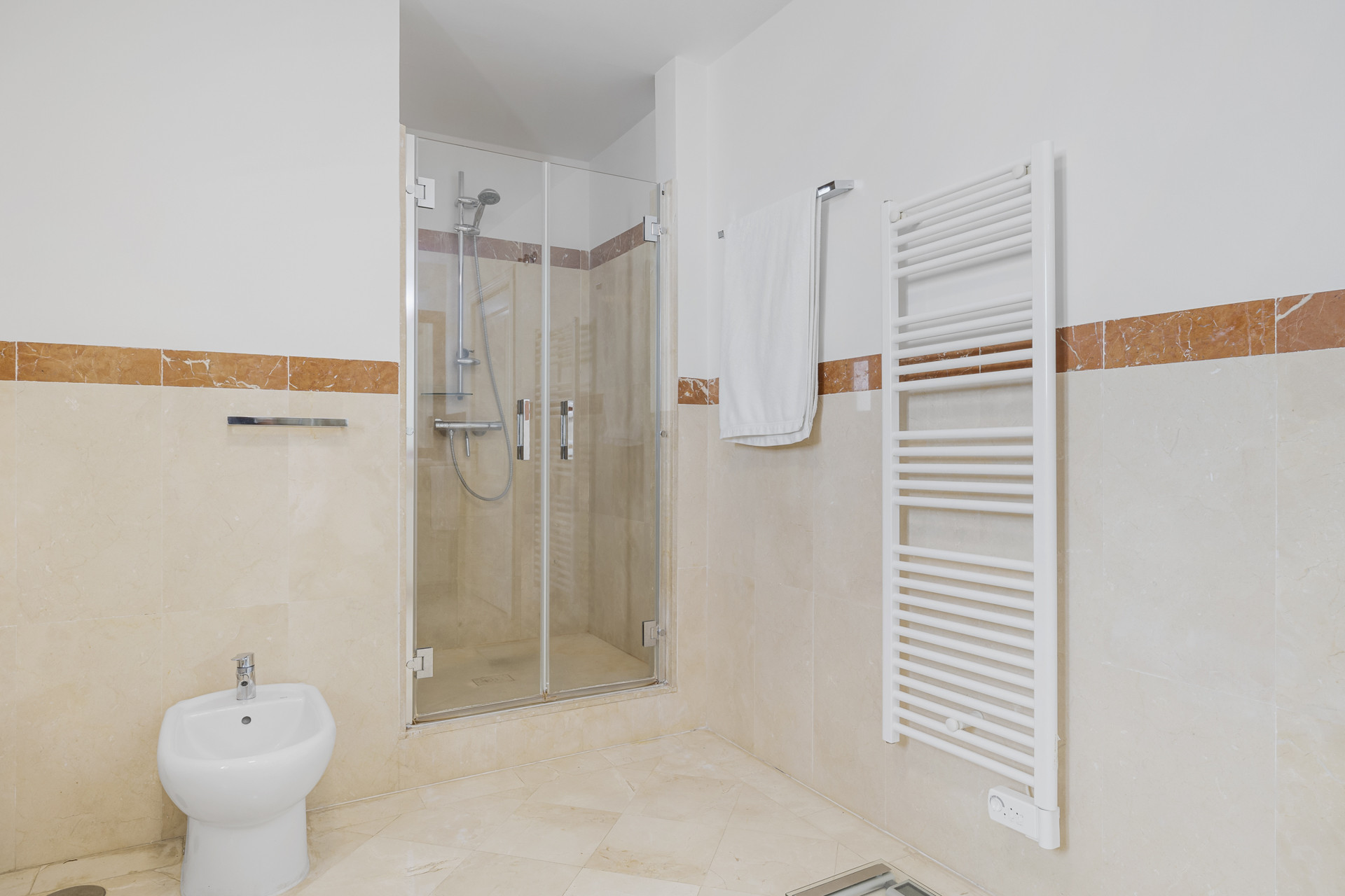 Bathroom with a glass shower, bidet, towel warmer, and brown tiled accent walls.