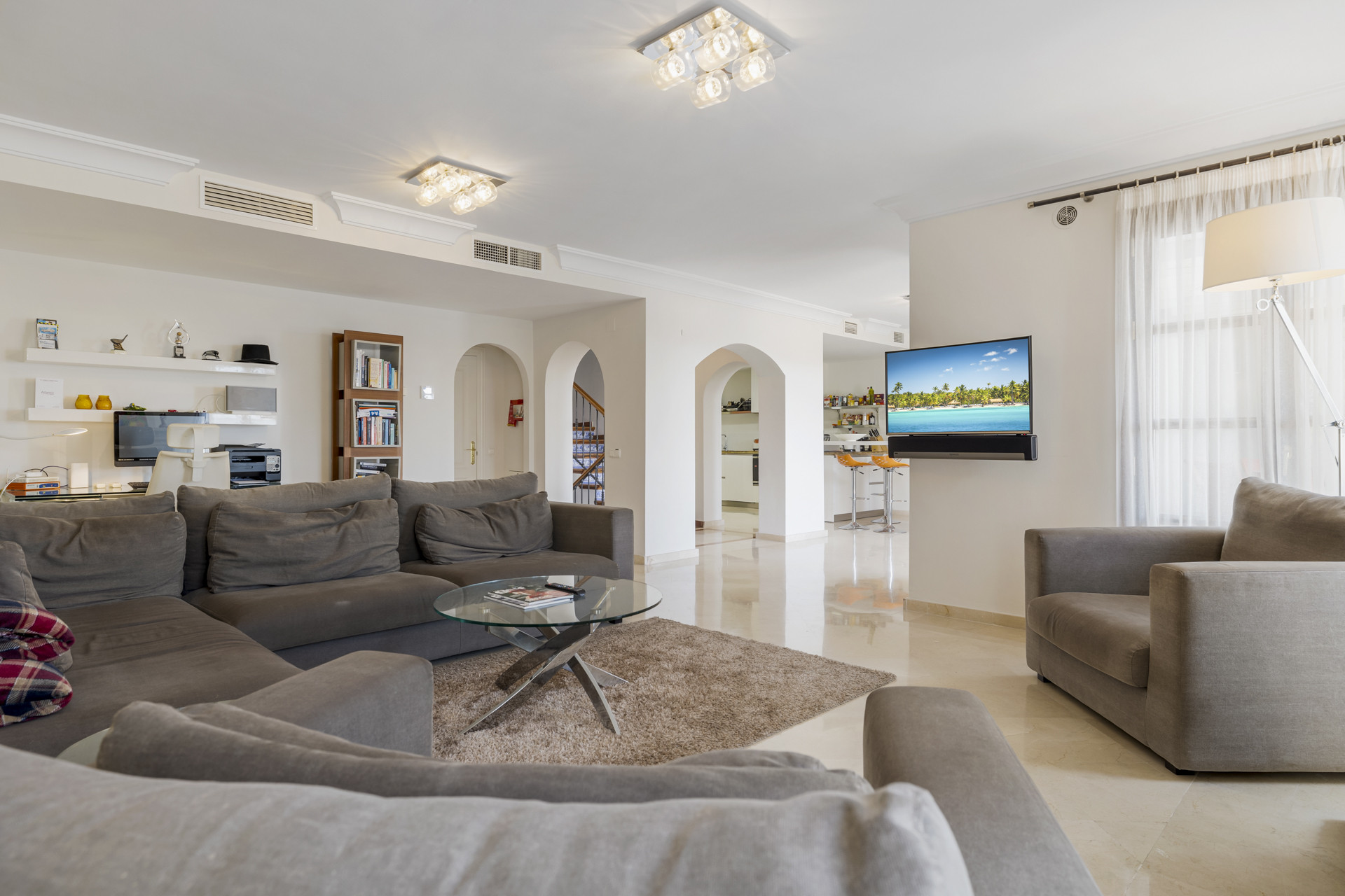 Living room with gray sectional sofa, glass coffee table, TV, and arched doorways to other areas.